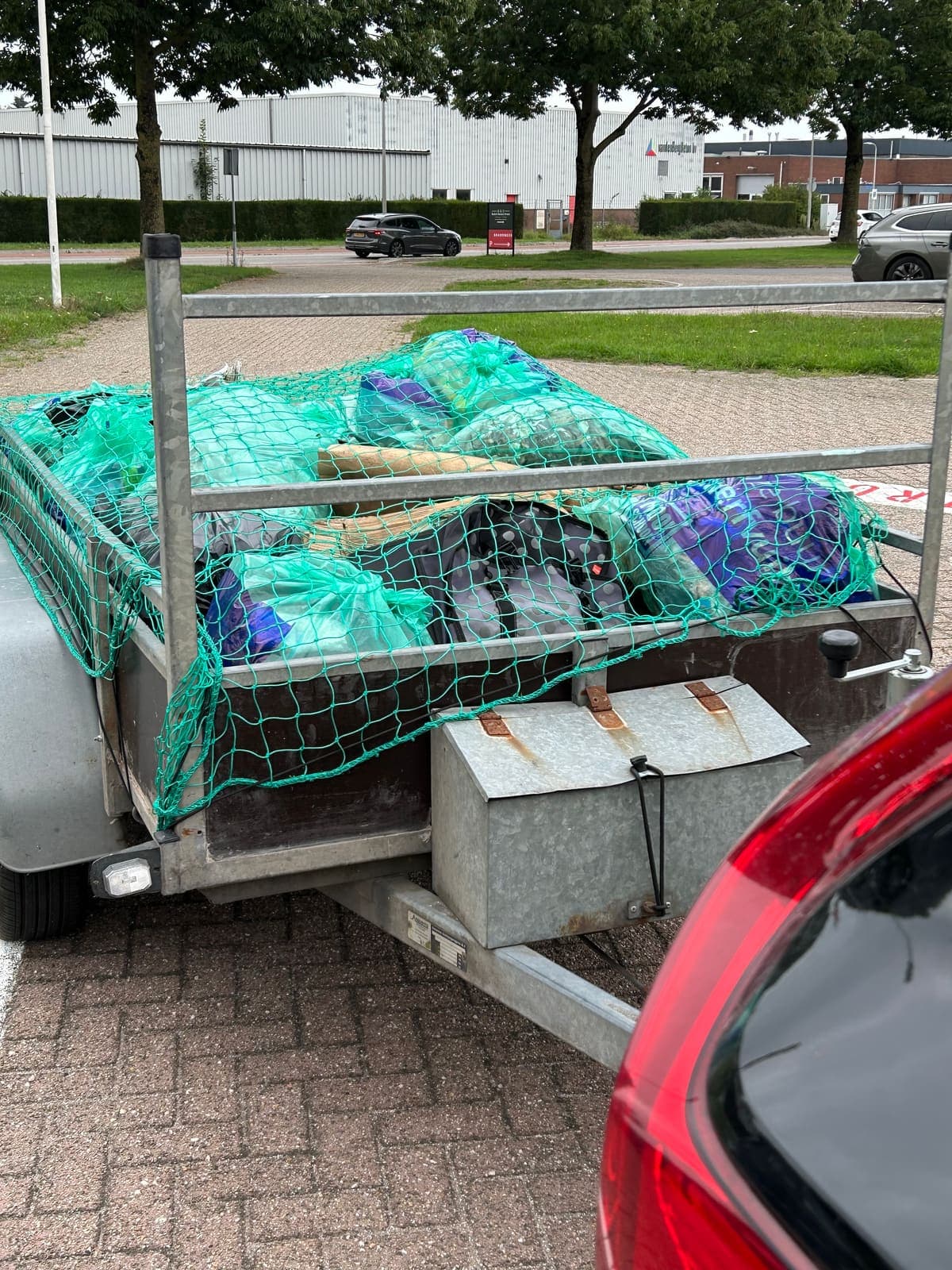 Een aanhanger vol groene en blauwe zakken met ingezameld zwerfafval, vastgezet onder een groen net.