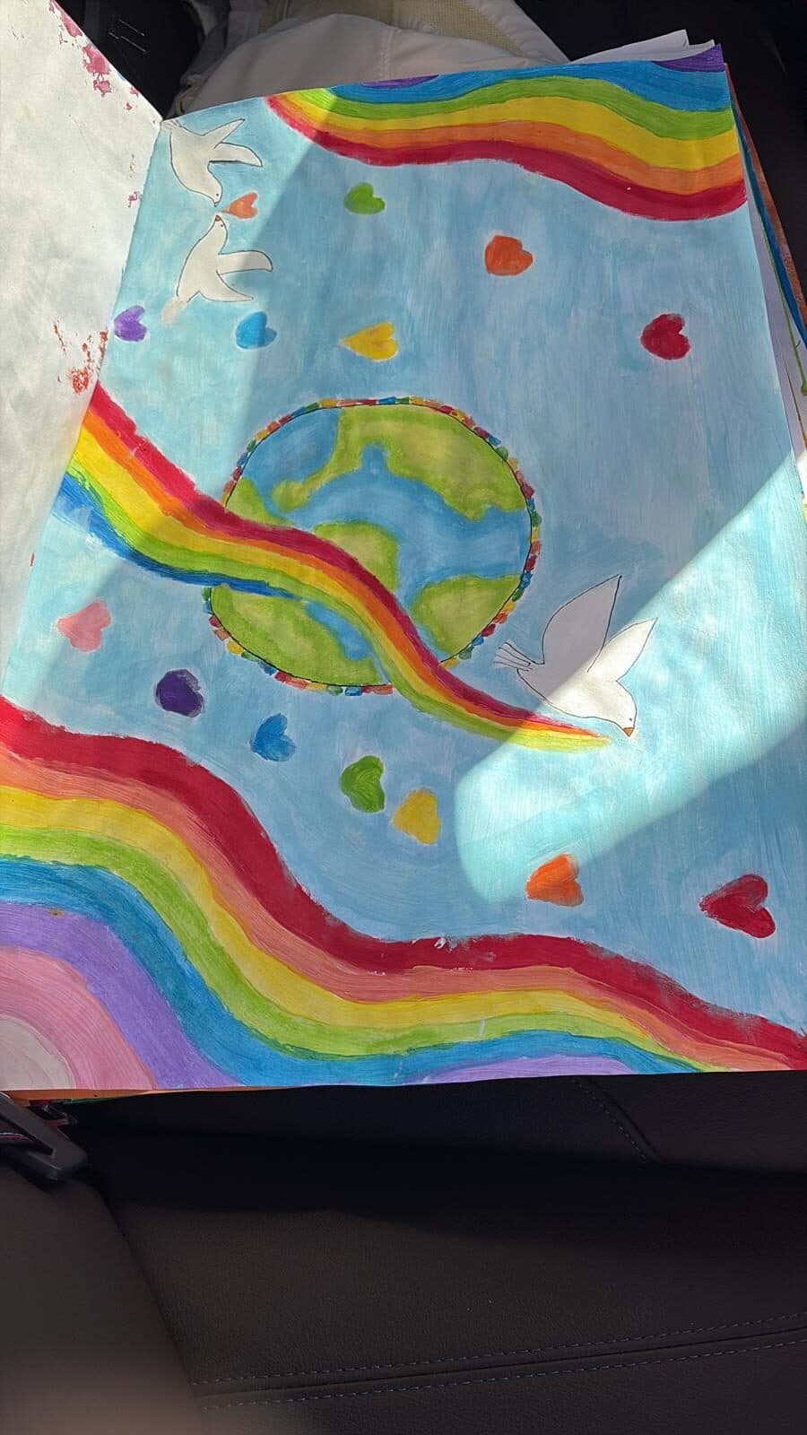 A painted peace poster with rainbows, white doves and coloured hearts around the globe.